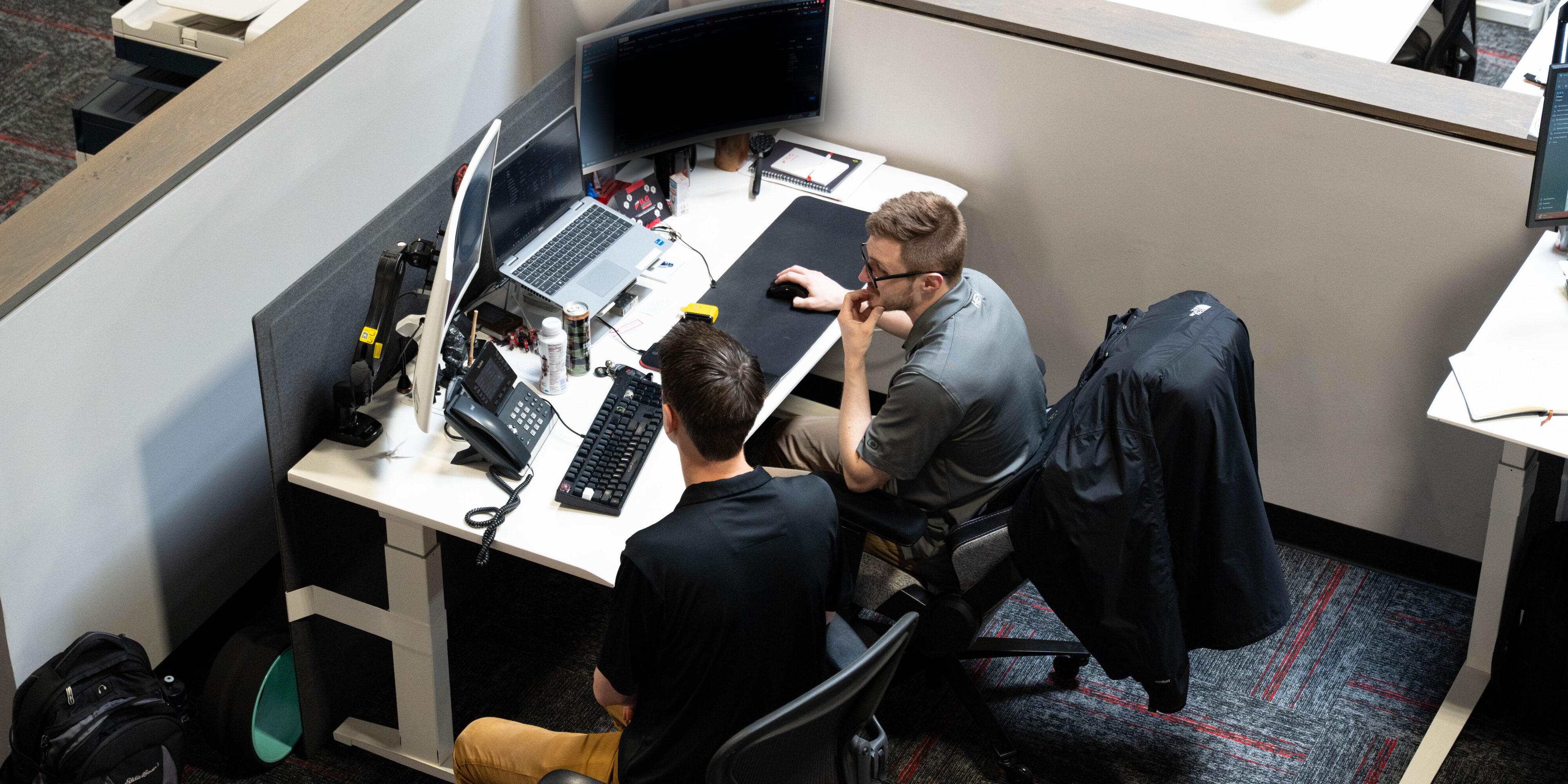 two men sitting at a computer desk staring at monitor screens